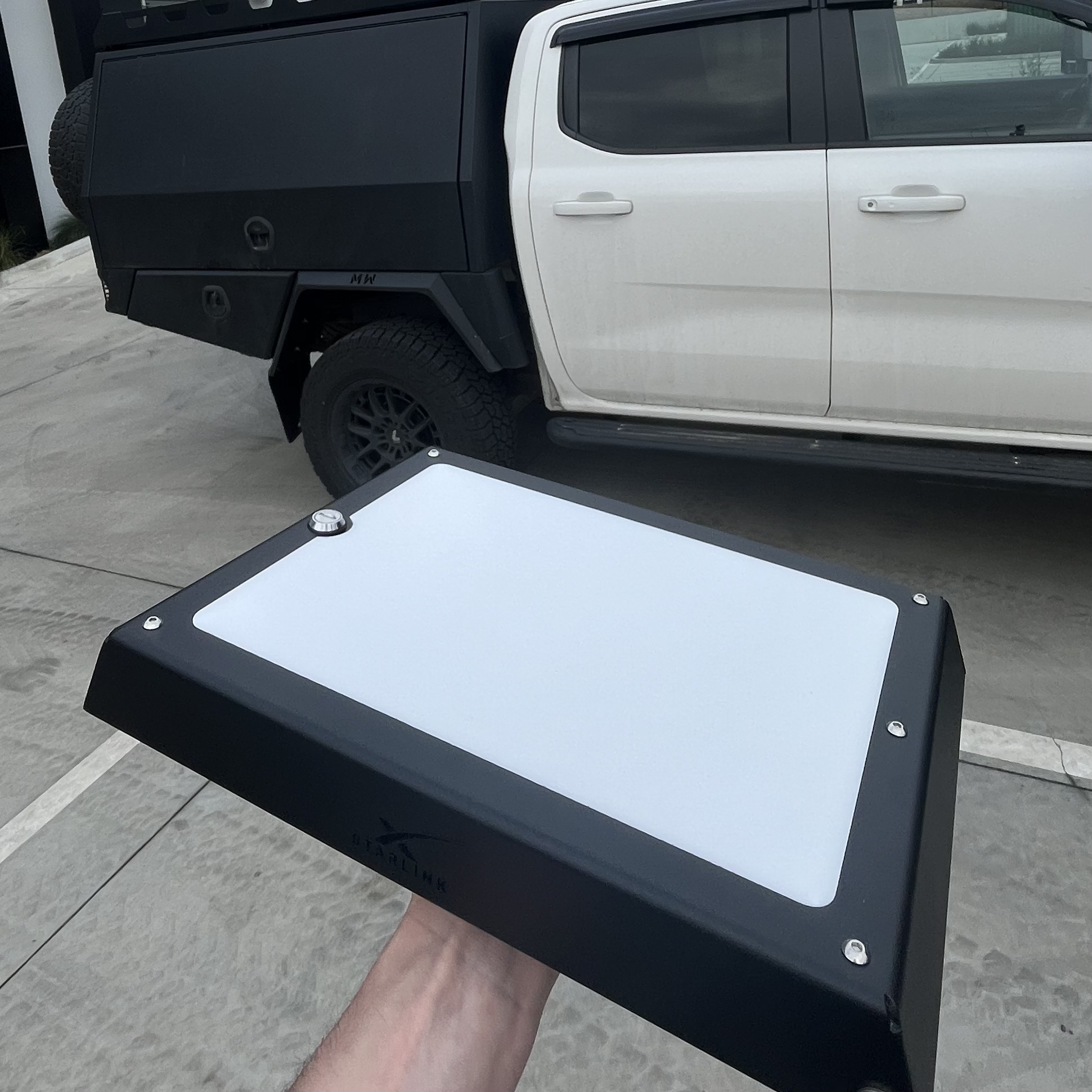 Black Fan-Cooled Rooftop Power Hub held beside a white dual-cab utility with a black tray, showing how the textured powder coat and low profile sit against the vehicle